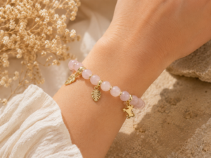 Bracelet en quartz rose porté au poignet avec breloques dorées
