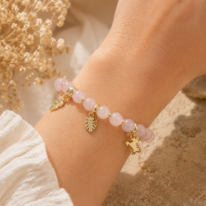 Bracelet en quartz rose porté au poignet avec breloques dorées